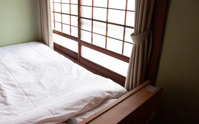 Bed beside shoji windows in Kawazoi room（障子窓のそばにある川沿いの客室のベッド）
