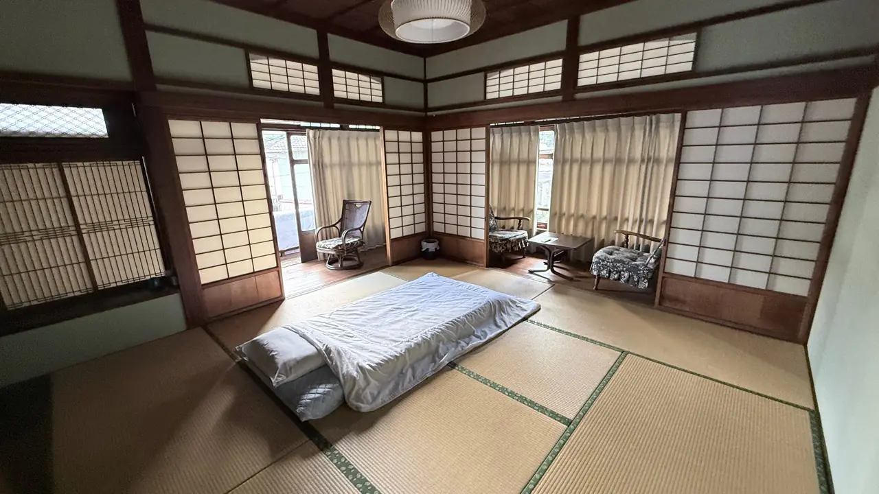 障子、畳、布団、窓辺の椅子を備えた梅の和室